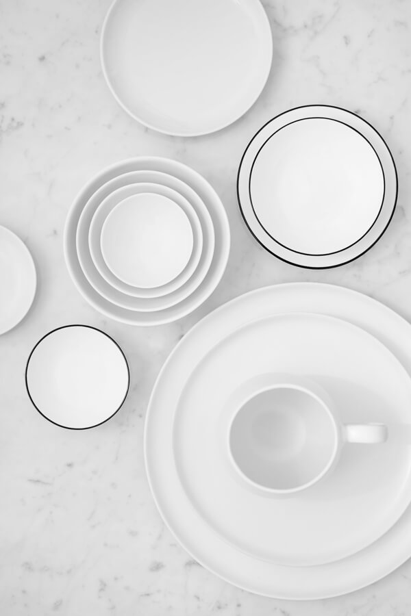 A simple flat lay with many white plates, bowls, and cups from Interio placed on a marble top.