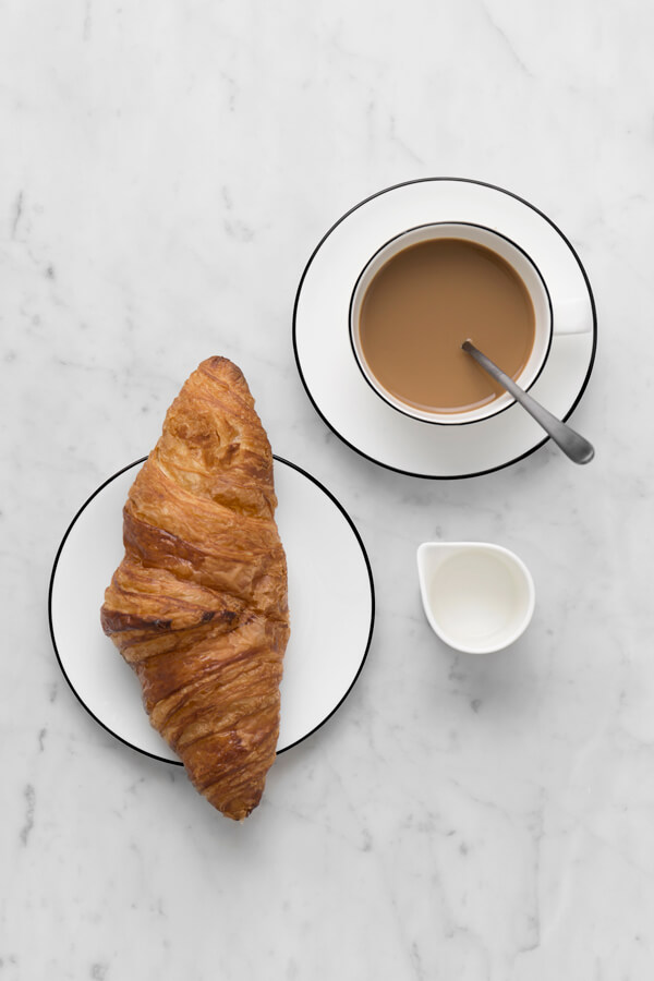 A flat lay with coffee, milk, a fresh croissant and tableware by Interio.